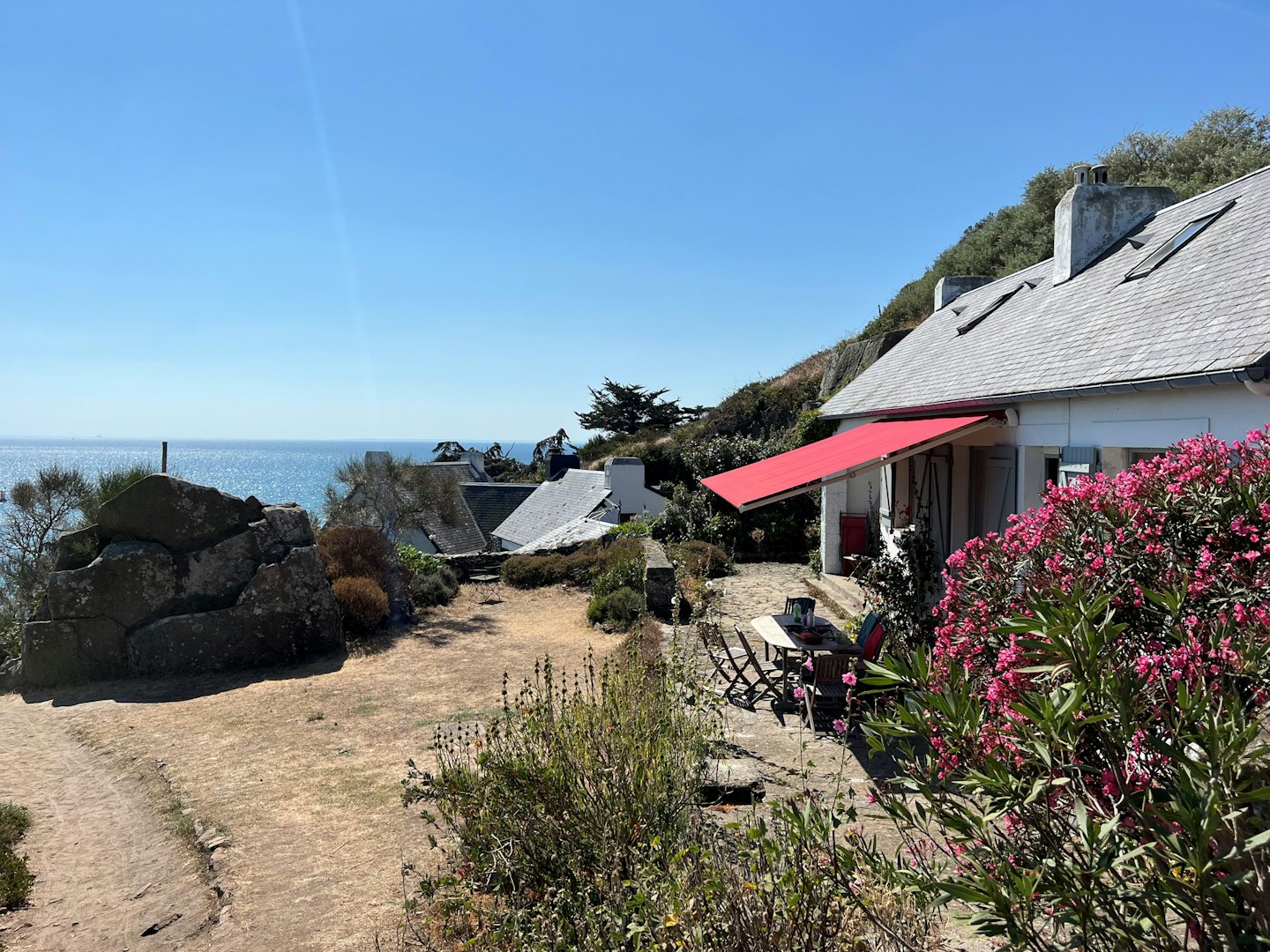 A white house with a red awning overlooks the ocean.