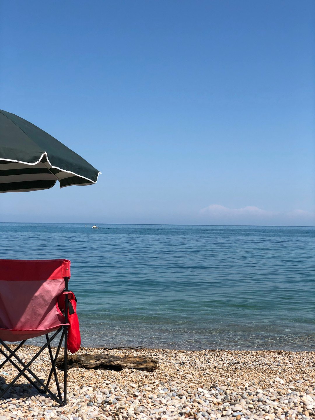 A striped umbrella and red chair sit on a pebble beach.