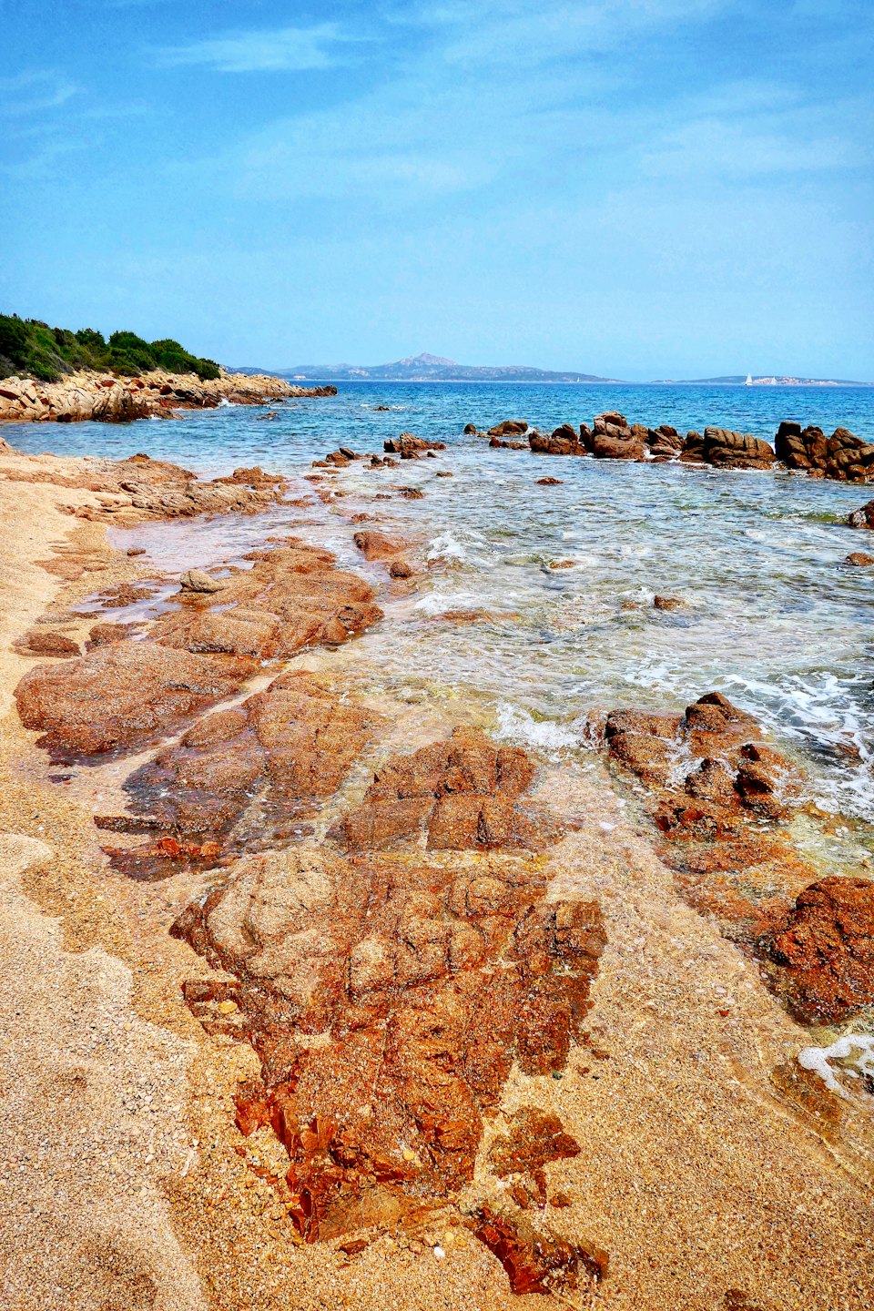 Clear ocean water flows over coastal rocks and sand.