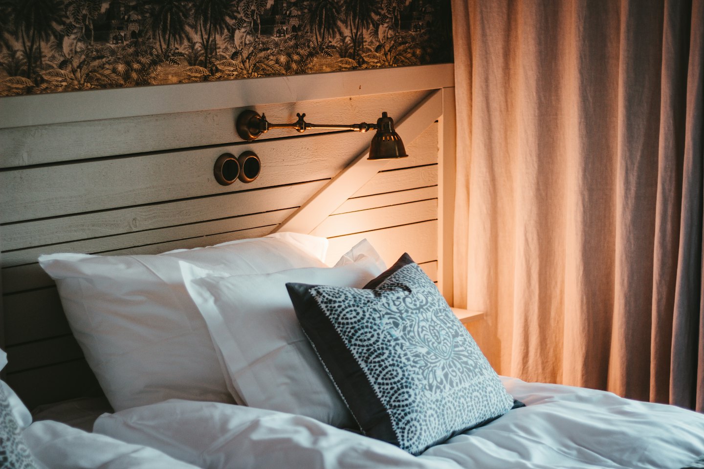 Cozy bedroom with tropical wallpaper and brass lamp.