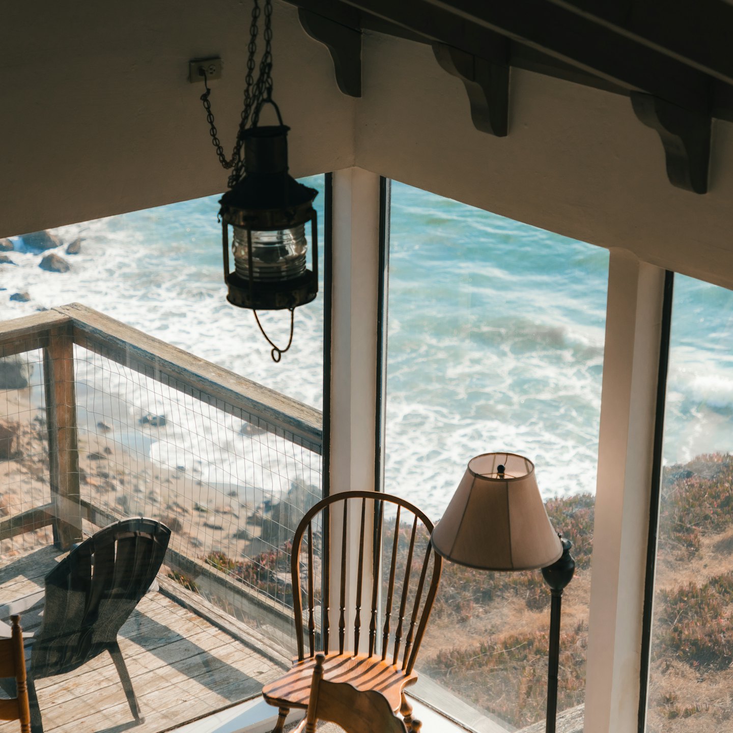 Wooden chair and lamp sit by windows overlooking the ocean.