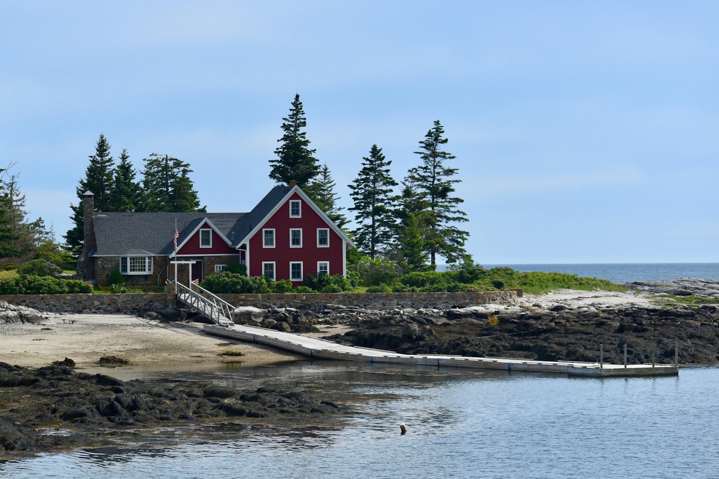 Red house on a rocky shoreline by the calm water.