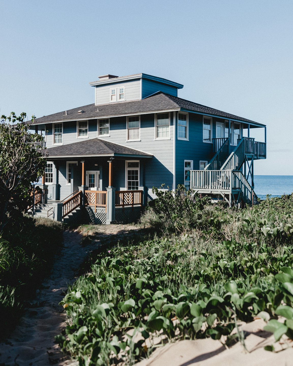 Light blue beach house with porch and balcony on a sandy dune.