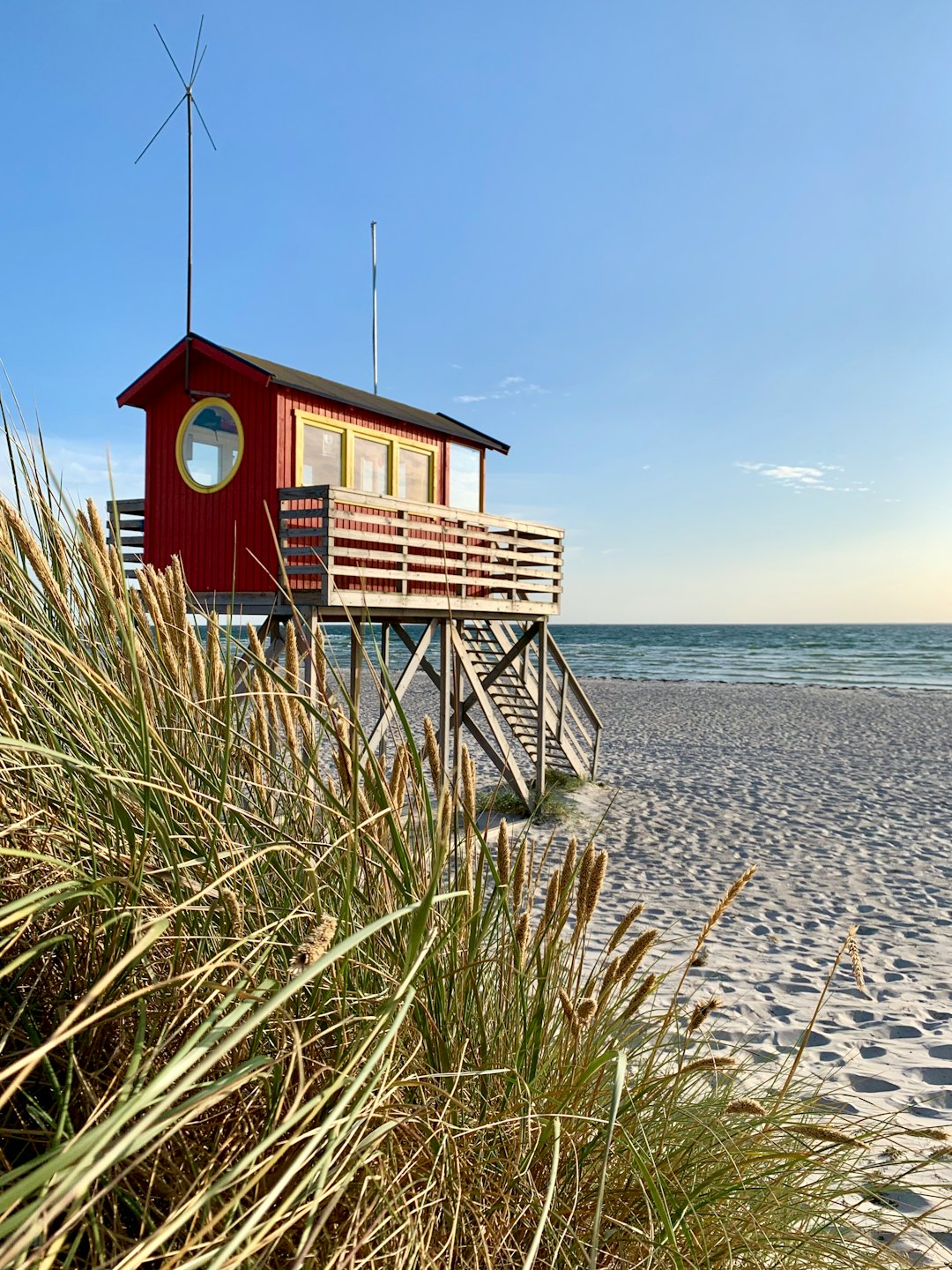 Red beach house on stilts stands above the sandy beach.